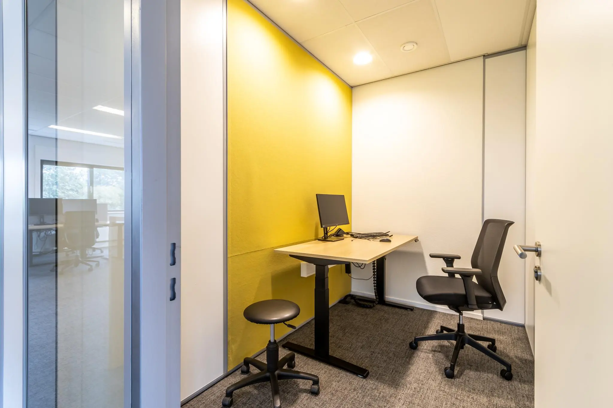 Kleine, moderne kantoorruimte aan de Lage Biezenweg met een bureau, bureaustoel en gele accentmuur.